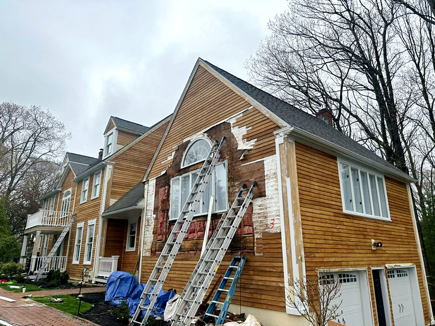 Cedar clapboard siding replacement project mid-job on Connecticut home, ladders staged for full-house repair