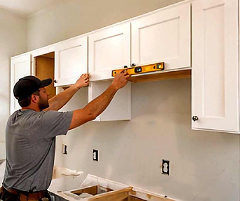 Carpenter setting upper kitchen cabinets with a level, Connecticut carpentry project