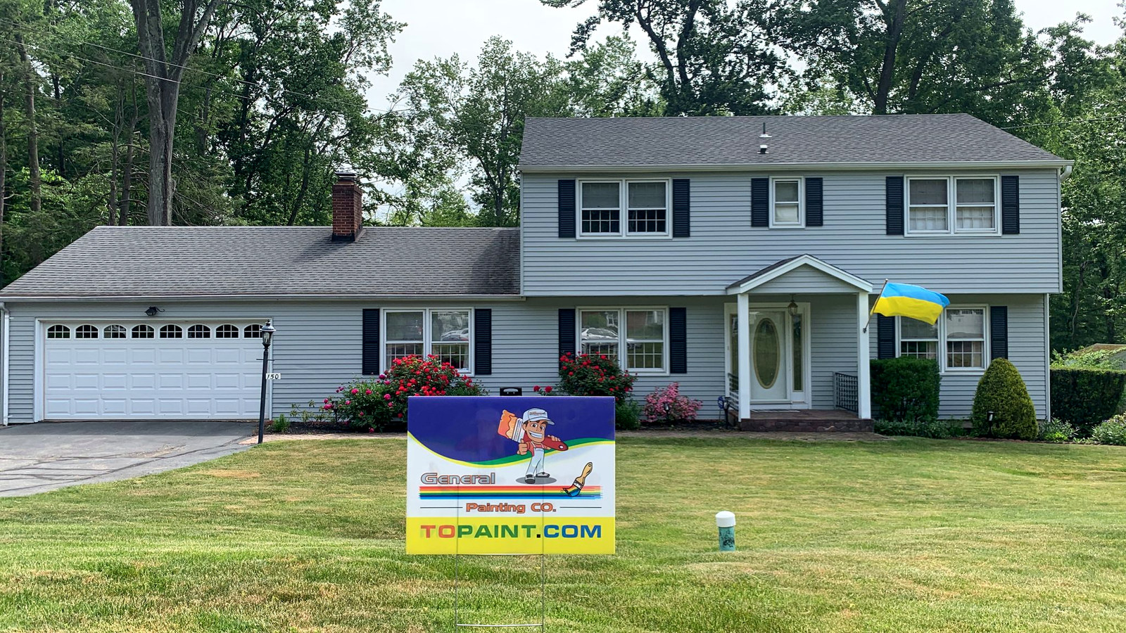 Blue-gray colonial home with vibrant flowers and yard sign in Connecticut