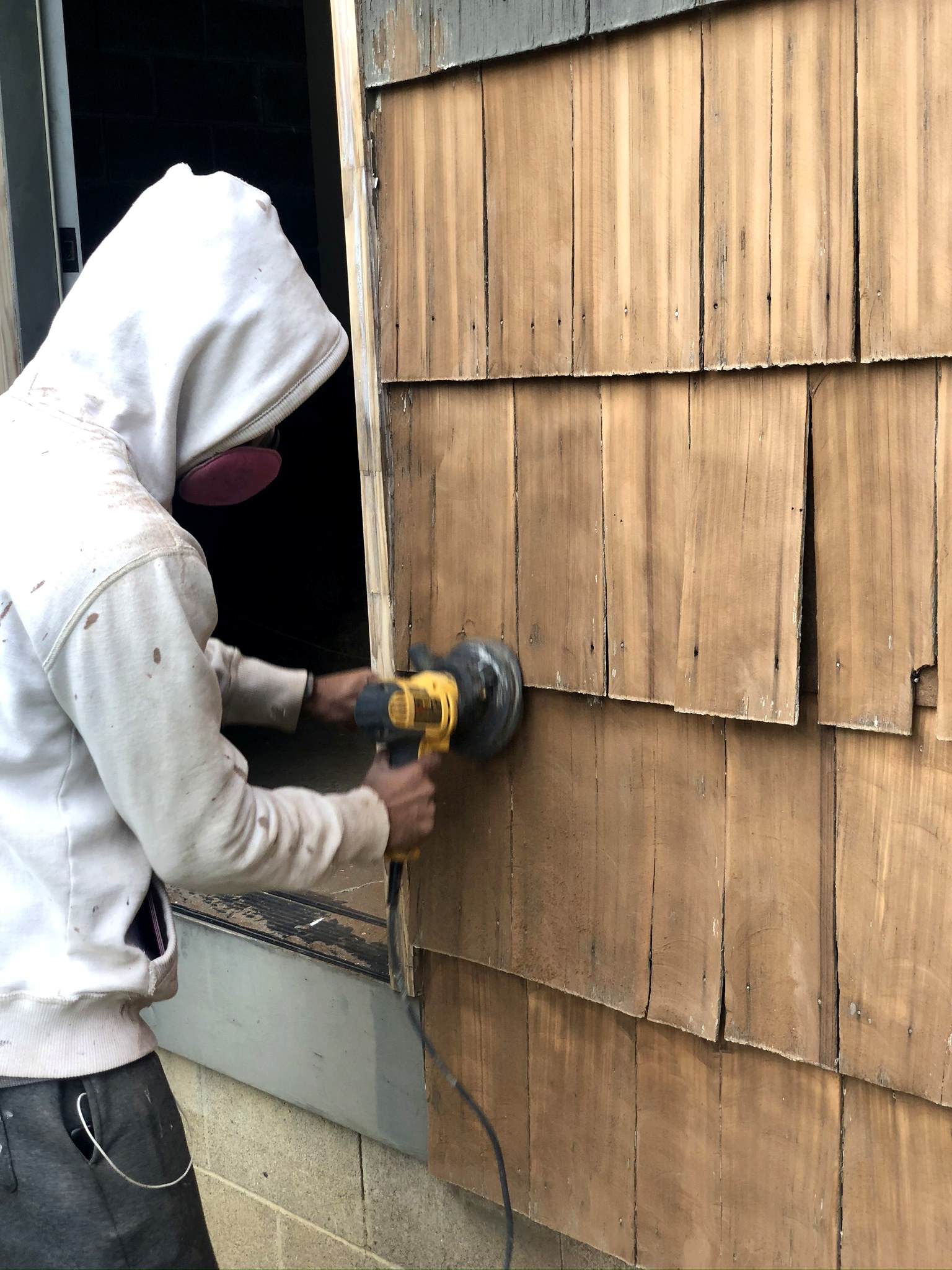 Worker sanding cedar shingle siding with proper safety mask