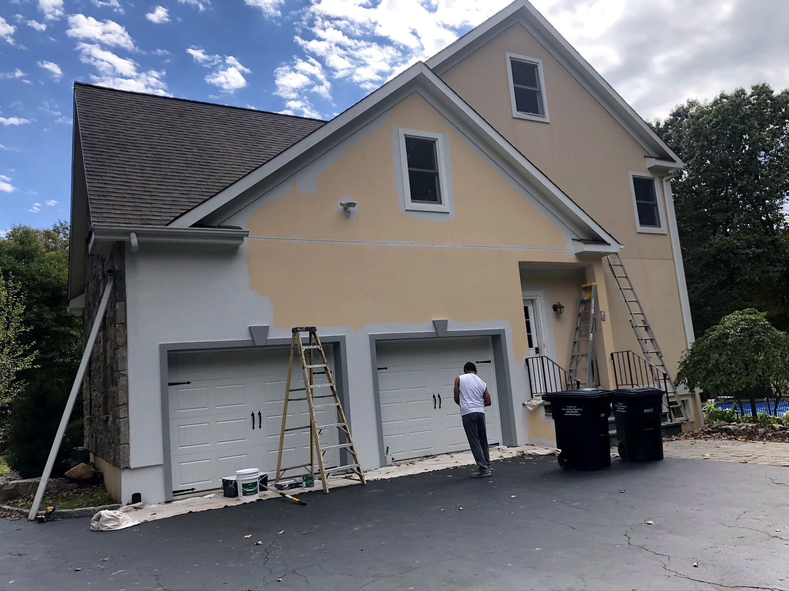 Stucco home mid-paint with ladders and crew in Connecticut