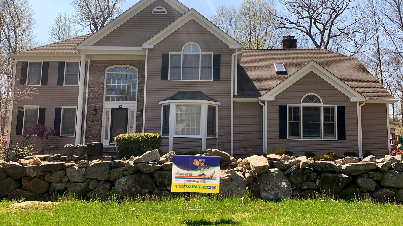 Beige colonial home with stone wall and General Painting Co. yard sign — finished exterior repaint